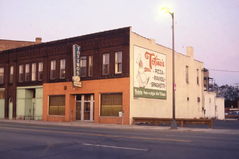 An old looking building based in the USA with a vintage Totino's Pizza sign under a street lamp.